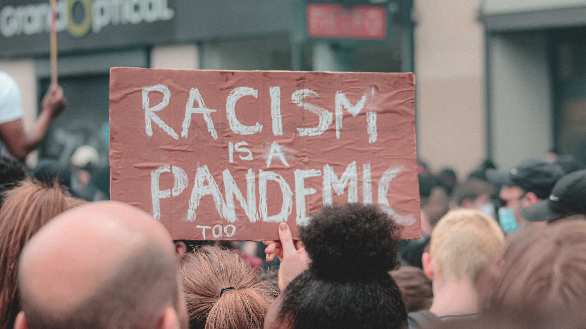 Schild bei einer Demonstration: "Racism is a Pandemic too"